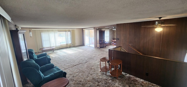 carpeted living room with wooden walls, a textured ceiling, and ceiling fan