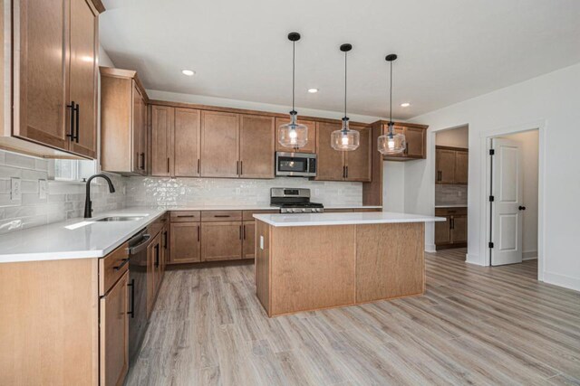 kitchen with a kitchen island, light wood-type flooring, stainless steel appliances, sink, and decorative light fixtures