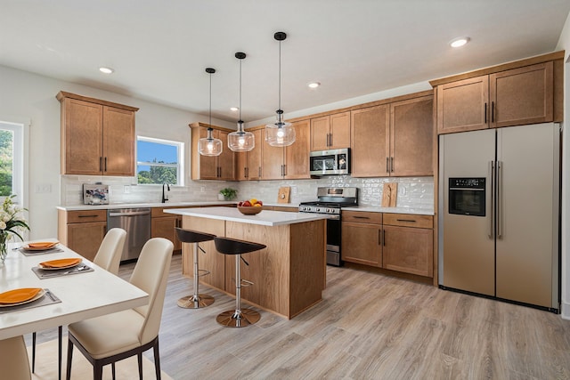 kitchen with light wood-type flooring, a kitchen island, hanging light fixtures, appliances with stainless steel finishes, and backsplash