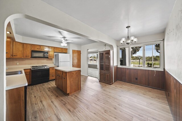 kitchen with hanging light fixtures, a kitchen island, light hardwood / wood-style flooring, wooden walls, and black appliances