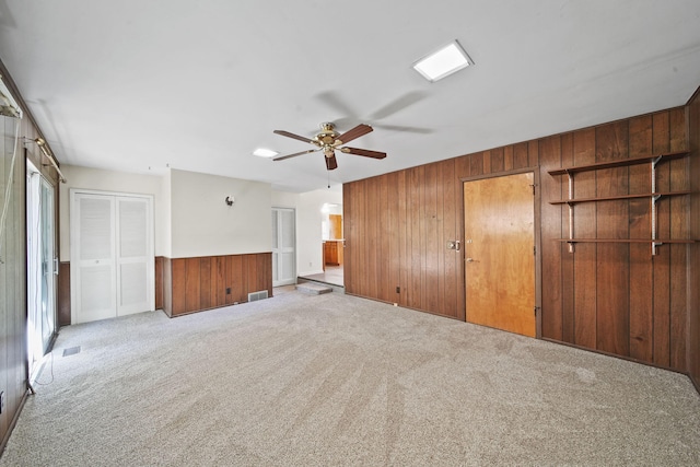 unfurnished bedroom with ceiling fan, light colored carpet, and wood walls