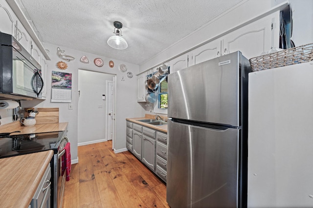 kitchen featuring stainless steel appliances, light wood-type flooring, hanging light fixtures, a textured ceiling, and sink