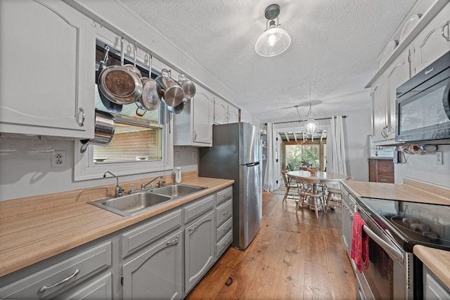 kitchen with hardwood / wood-style floors, pendant lighting, sink, a textured ceiling, and stainless steel appliances