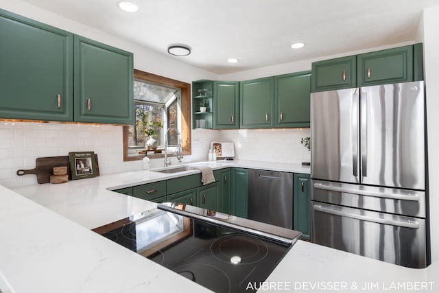 kitchen with green cabinets, light stone counters, sink, and stainless steel refrigerator