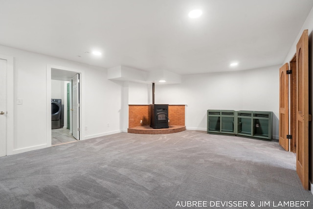 unfurnished living room featuring washer / dryer, light carpet, and a wood stove