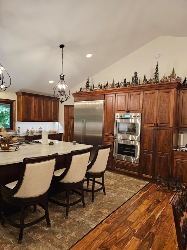 kitchen with pendant lighting, lofted ceiling, appliances with stainless steel finishes, an inviting chandelier, and dark hardwood / wood-style flooring