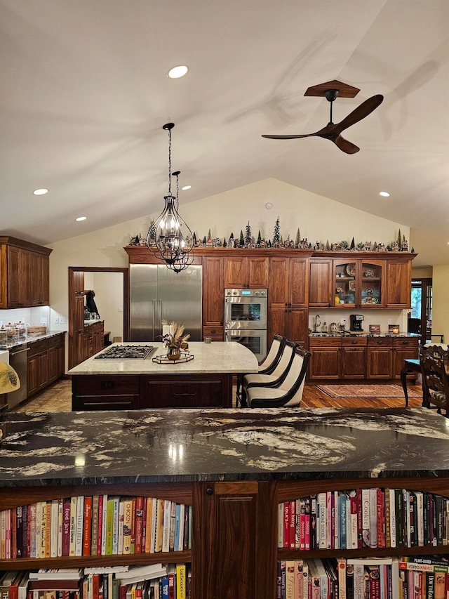 kitchen with pendant lighting, dark stone counters, dark hardwood / wood-style flooring, vaulted ceiling, and stainless steel appliances