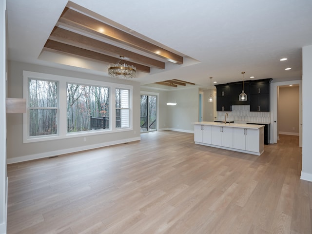 unfurnished living room featuring sink, an inviting chandelier, beamed ceiling, and light wood-type flooring