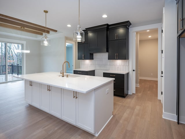 kitchen featuring sink, light wood-type flooring, a kitchen island with sink, and hanging light fixtures