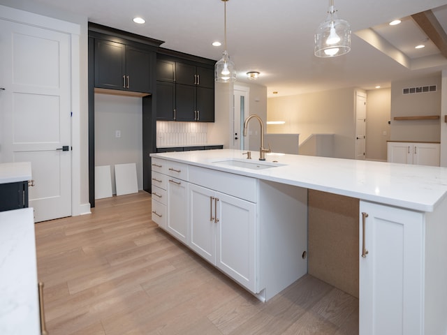 kitchen featuring sink, light stone counters, pendant lighting, light hardwood / wood-style floors, and decorative backsplash