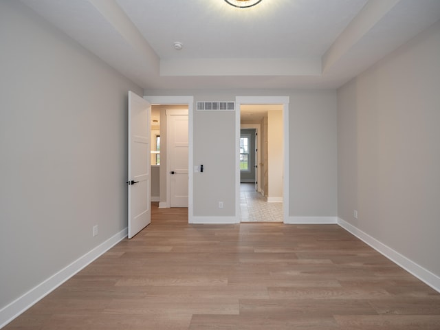 unfurnished bedroom with light hardwood / wood-style floors and a tray ceiling