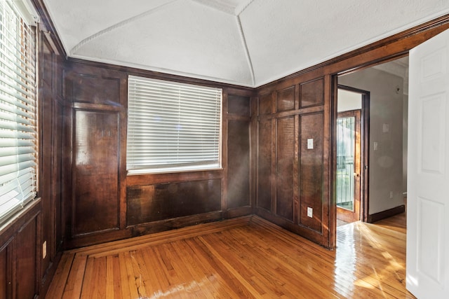 unfurnished room featuring lofted ceiling, a wealth of natural light, light hardwood / wood-style floors, and a textured ceiling