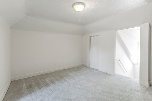 additional living space featuring light carpet, a textured ceiling, and vaulted ceiling