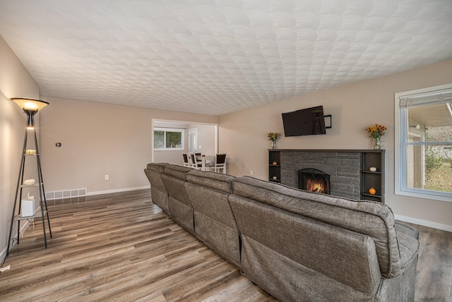 living room featuring hardwood / wood-style flooring, plenty of natural light, and a stone fireplace