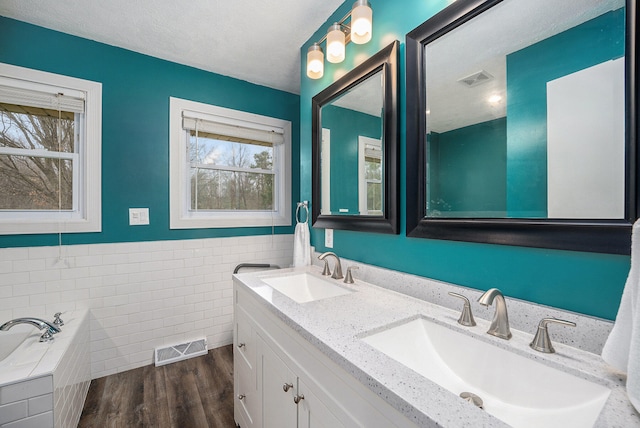 bathroom featuring hardwood / wood-style floors, vanity, a tub to relax in, and tile walls