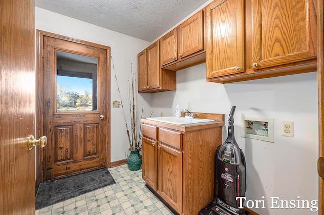 clothes washing area with a textured ceiling, washer hookup, sink, and cabinets