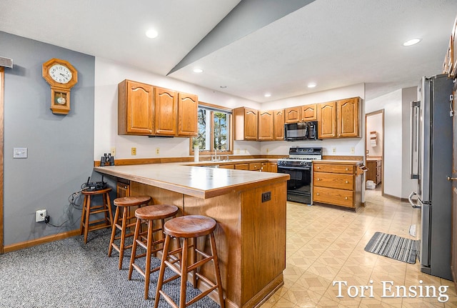 kitchen with black appliances, sink, kitchen peninsula, vaulted ceiling, and a kitchen bar