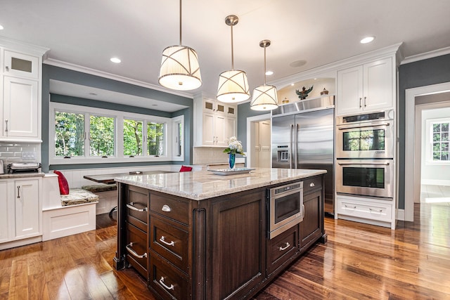 kitchen featuring tasteful backsplash, dark brown cabinets, built in appliances, white cabinetry, and hanging light fixtures