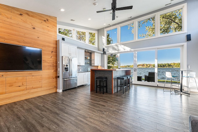 kitchen with white cabinetry, a kitchen breakfast bar, stainless steel refrigerator with ice dispenser, wooden walls, and a water view