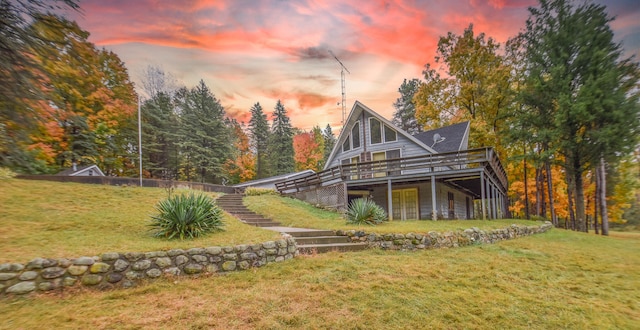 back house at dusk featuring a wooden deck and a lawn