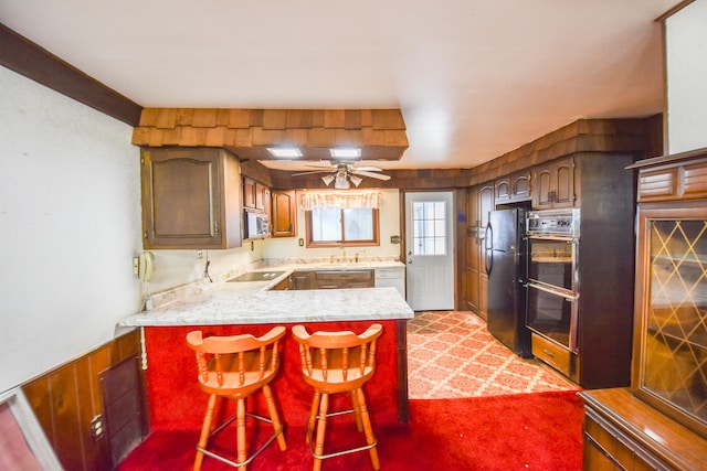 kitchen with ceiling fan, sink, kitchen peninsula, black appliances, and a kitchen bar