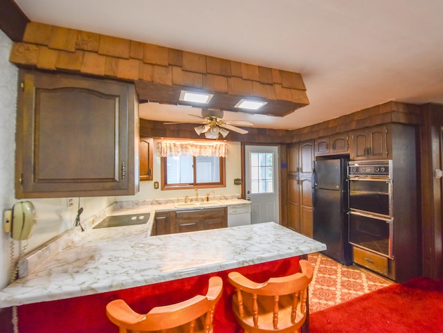 kitchen with ceiling fan, sink, kitchen peninsula, black appliances, and a breakfast bar