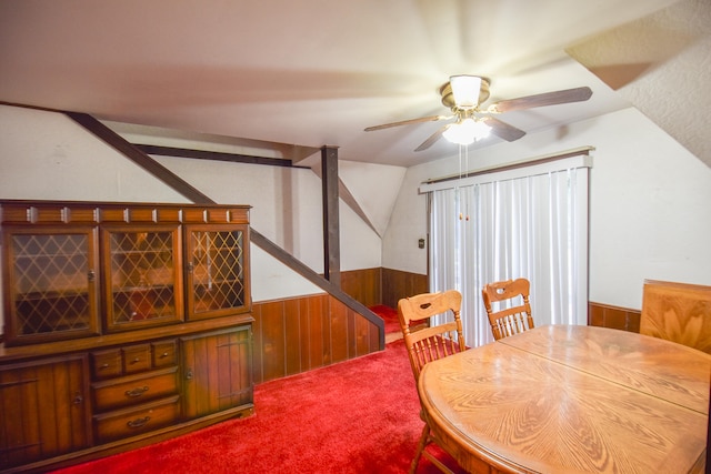 carpeted dining space featuring wood walls, vaulted ceiling, and ceiling fan