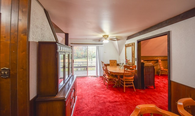 carpeted dining space featuring ceiling fan and wooden walls