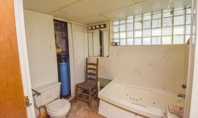 bathroom with a tub to relax in, a drop ceiling, and toilet