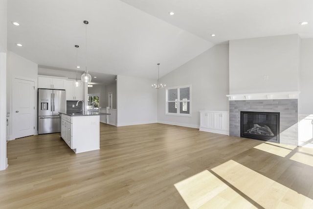 unfurnished living room featuring a tiled fireplace, an inviting chandelier, sink, and light hardwood / wood-style floors