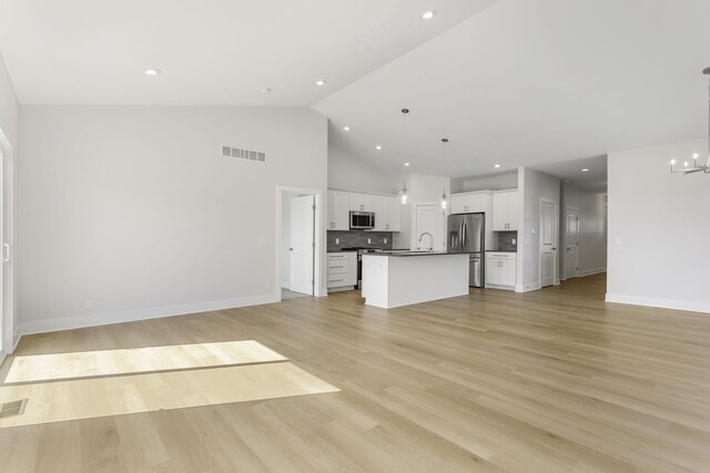 unfurnished living room with a notable chandelier, high vaulted ceiling, sink, and light hardwood / wood-style flooring