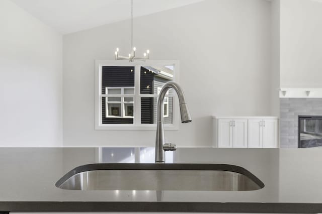 room details with white cabinets, hanging light fixtures, sink, an inviting chandelier, and a fireplace