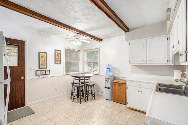 kitchen with beam ceiling, white cabinetry, sink, and a textured ceiling