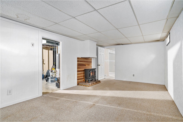 unfurnished living room with a wood stove, a paneled ceiling, and carpet flooring