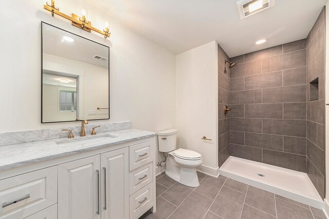 bathroom featuring vanity, a tile shower, toilet, and tile patterned flooring