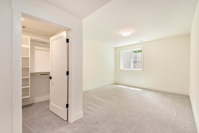 unfurnished bedroom with light carpet, a closet, and a spacious closet