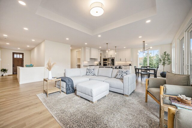 living room with a notable chandelier, light wood-type flooring, and a raised ceiling