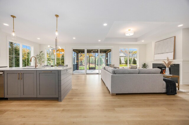 living room with light hardwood / wood-style floors, a raised ceiling, sink, and a chandelier