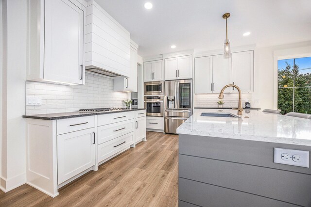 kitchen with white cabinetry, light hardwood / wood-style flooring, dark stone countertops, built in appliances, and sink