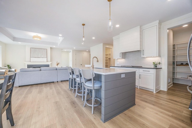 kitchen with light wood finished floors, a sink, backsplash, premium range hood, and white cabinets