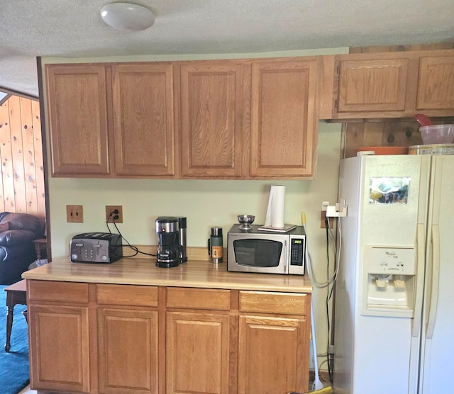 kitchen featuring a textured ceiling and white refrigerator with ice dispenser