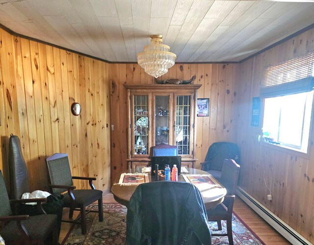 dining area featuring wood-type flooring, a notable chandelier, wooden walls, and a baseboard heating unit