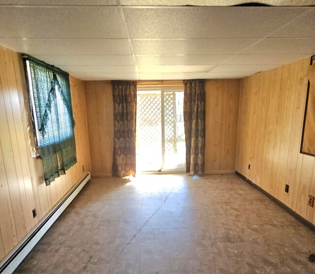 empty room featuring wood walls, a drop ceiling, and baseboard heating