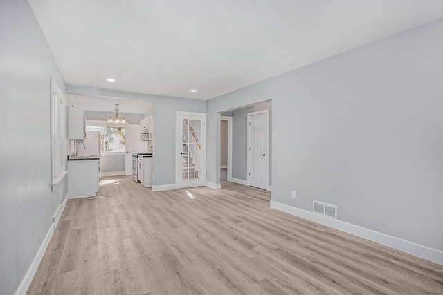 unfurnished living room with light wood-type flooring and a notable chandelier