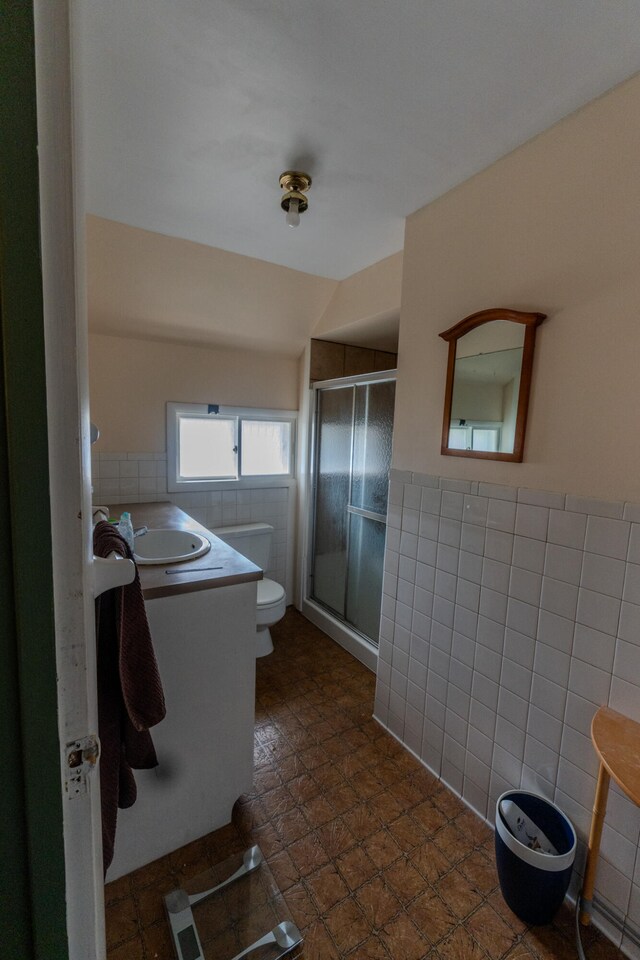 bathroom with tile patterned flooring, toilet, tile walls, a shower with door, and vanity