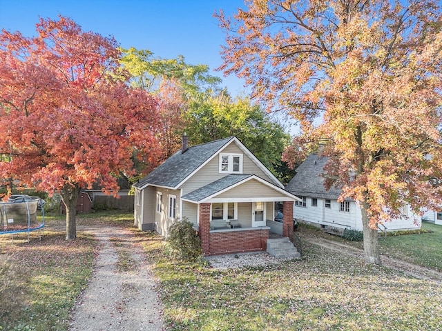 bungalow-style home featuring a porch, a front lawn, and a trampoline