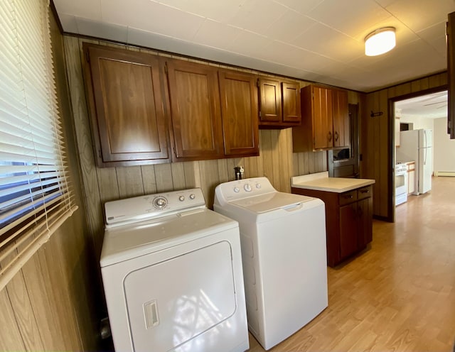 clothes washing area with wood walls, washing machine and clothes dryer, light hardwood / wood-style flooring, a baseboard heating unit, and cabinets