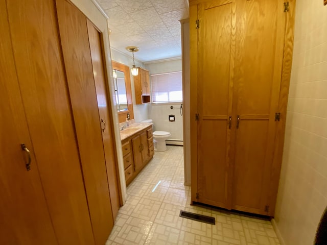 bathroom with toilet, crown molding, baseboard heating, tile walls, and vanity