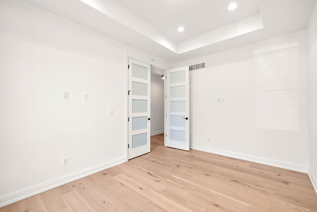 unfurnished room with a tray ceiling and light wood-type flooring