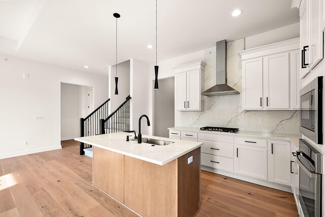 kitchen featuring white cabinets, an island with sink, light wood-type flooring, wall chimney exhaust hood, and sink